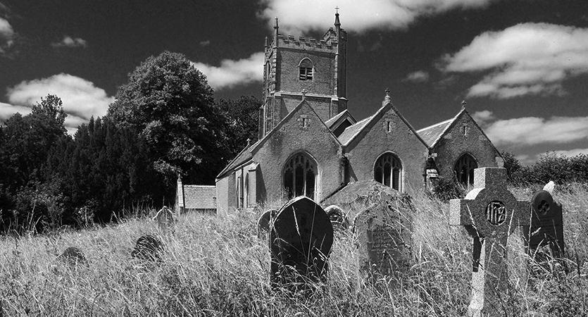 Monochrome image of Landulph Church looking across the graveyard, with dramatic skies 